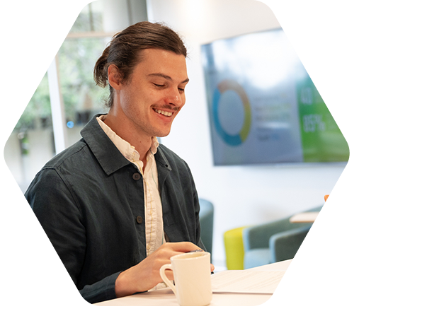 Smiling man looks at paper on table while another man in dress shirt and glasses listens